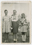 Lenka, Bluma and Malka Gruenberg stand in a field in Cierny Potok holding flowers.