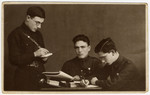 Close-up studio portrait of three members of Betar Latvia writing at a desk.