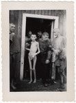 Survivors, some undressed, stand by a barrack door after liberation.
