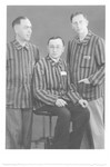 Three survivors pose for a studio portrait in their camp uniforms after liberation.