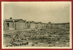 Photograph showing debris outside a row of barracks in the Dachau concentration camp pasted into an album presented to Lt.