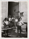 Several young boys help move classroom furniture--a table, a bench, and a chair--outside, at the Rivesaltes internment camp.