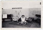 A young girl interned at Rivesaltes sits on the floor of a play room,  fiddling with her dolls.