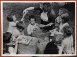 A group of children gather around their caretaker as they open packages filled with toys.