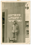 A young Jewish displaced person poses [perhaps in his camp uniform] in front of a memorial to the victims of the Holocaust.