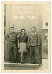Three Jewish displaced persons pose in front of a memorial to the victims of the Holocaust.