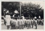 Young children led by young women stand at attention at a flag raising.