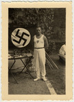 A German athlete stands next to a Nazi flag and a table with Mein Kampf.