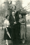 A group of four woman and one man pose by a tree.