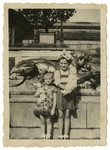 Renee Schwalb and a younger friend stand holding their dolls nex to a statue.