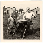 Herbert Hoexter and another gentleman sit outside at a small table in the Kitchener refugee camp.