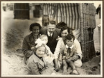A German-Jewish family relaxes on the beach in front of a cabana.