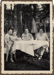Three women gather at an outdoor table.

From left to right are Ilse Baruch holding her son Peter, her sisters-in-law Thekla Erdman and Marianne Ziegler.