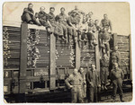 Jewish internees pose on top and next to a railcar loaded with planks of lumber in Westerbork.