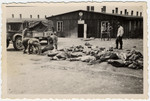 Survivors of Buchenwald clear corpses from the road in front of Barracks #17, as some American soldiers look on.