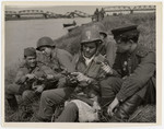 Soviet and American soldiers show each other their pistols while relaxing on the banks of the Elbe River.