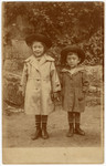 The young siblings, Ilse and Hans Heinz Hanauer, hold hands outside in their trench coats and hats.