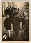 A woman walks down a street in prewar Lodz with her two children.