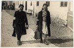 Two young women wearing armbands walk down a street near the town square in the Bolechow ghetto.