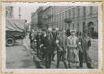 A group of Jewish men wearing armbands and some carrying shovels marches off for a labor assignment in an unidentified Polish city.