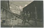 Two survivors of the Buchenwald concentration camp walk between the barracks in front of the barbed wire fence following liberation.