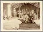 Patients [possibly POWs, ] and German medical officers inside a wooden hospital room.