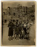 A  Greek Jewish family poses in front of a building in ruins.