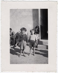 Several young Roma children wait outside a building (presumably a school) in the Rivesaltes internment camp.