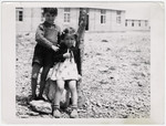 A Spanish boy and girl stand outside next to a tree, in front of a school building at Rivesaltes.