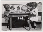 A small group of Spanish children sit at a table in the Rivesaltes internment camp, playing with blocks.