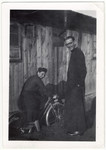Madeleine Barot riding a bicyle and a Christian clergyman [probably Father Dumas] pose outside of a building in the Gurs internment camp.