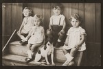Four young Jewish children sit on the steps to a house with their dog.
