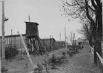 View of a section of the Ohrdruf concentration camp that includes a watchtower, barracks, and barbed wire fencing.