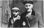 Two Jewish men wearing yellow stars stand in front of a shuttered store in an unidentified ghetto in Poland.