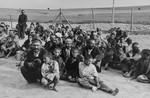 A group of Romani prisoners, awaiting instructions from their German captors, sit in an open area near the fence in the Belzec concentration camp.