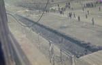 View from above of former prisoners walking along the main street of the newly liberated Dachau concentration camp parallel to the moat and the barbed wire fence.