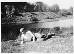 Jeannot, a young boy rescued by the priest Edouard Robert, lies down on the banks of a river.