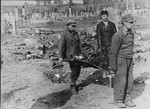 Under the supervision of a Soviet policeman, the charred remains of Jews from the Kovno ghetto are carried on a makeshift stretcher to a mass grave.