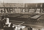 Members of the BDM (Bund deutscher Maedels) stand in formation in the bleachers of the Berlin stadium to spell out "Wir gehoeren dir!" [We belong to you] while Adolf Hitler delivers an address at a rally held on the National Day of the German People (May Day).