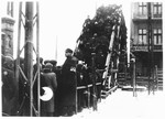 A Jewish policeman stands guard while Lodz ghetto residents wait in line to cross one of the pedestrian bridges.