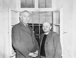 Dr. Adolf Wahlmann (left), chief physician at the Hadamar Institute, and Karl Willig (right), assistant male nurse, pose next to a barred window at the euthanasia facility where they are being held prisoner by American authorities.