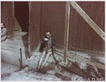 An emaciated survivor drinking from a metal bowl in front of a barracks in Buchenwald.