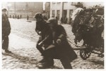Two men haul a full cart along a cobblestone street in the Lodz ghetto.