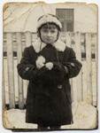 Portrait of a girl in a winter coat standing in front of a wooden fence.