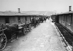 Horse-drawn wagons line up alongside a row of barracks in the Gusen concentration camp.