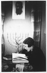 A young Jewish woman sits reading a book under a hanging portrait of Theodor Herzl.