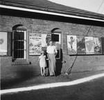A Jewish refugee father poses with his daughter in front of a building covered with travel posters in Kenya.