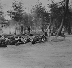 View of the Bergen-Belsen concentration camp shortly after liberation, with corpses lying in the foreground and survivors in the background.