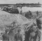 A British bulldozer closes a mass grave at Bergen-Belsen while former camp guards look on.