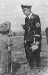 Reichsfuehrer-SS Heinrich Himmler converses with two children who have just presented him with a bouquet of flowers.